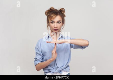 Ritratto di donna bionda che fa pausa o pausa gesto tempo, segno di timeout, chiedere di attendere, sconvolto circa scadenza, limite di tempo, indossare una camicia blu. Studio in interni isolato su sfondo grigio. Foto Stock