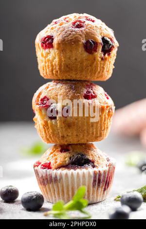 Muffin appena sfornati con zucchero a velo e frutti di bosco freschi. Muffin fatti in casa con mirtilli freschi e lamponi su sfondo chiaro. Fatto in casa b Foto Stock