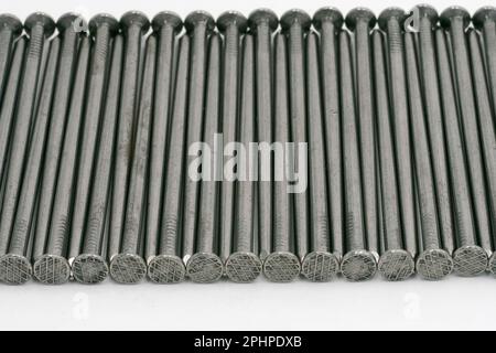 Chiodi metallici ordinatamente impilati su uno sfondo bianco Foto Stock
