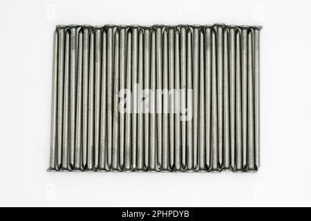 Chiodi metallici ordinatamente impilati su uno sfondo bianco Foto Stock