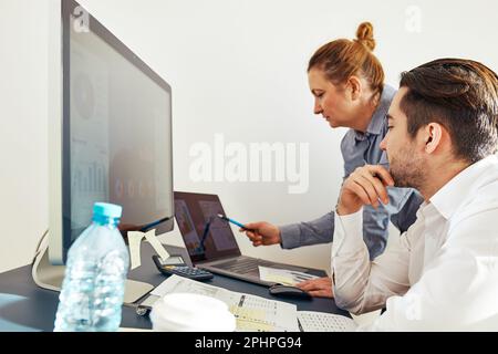 Colleghi aziendali che discutono di dati finanziari che lavorano insieme in ufficio. Persone imprenditori che lavorano con grafici e tabelle sul computer. Due persone Foto Stock