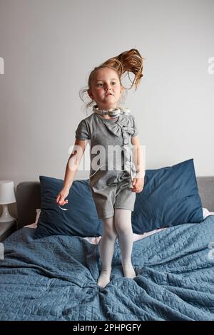 Bambina che canta con cuffie e cavo imitandosi una vera cantante. Bambino che ha divertimento ballare saltando ascoltando la musica sul letto in camera da letto a. Foto Stock