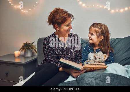 Mamma che legge libro sua figlia a letto prima di andare a dormire. Leggere storie prima di dormire. Storie di sonno per i bambini Foto Stock