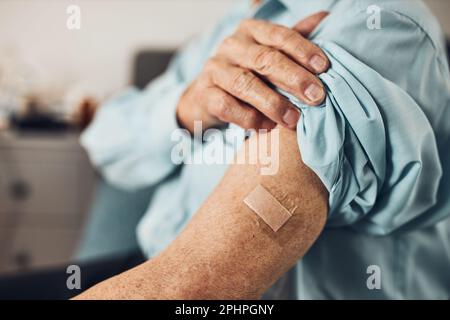 Paziente anziano che tiene la camicia manica in su con un gesso al posto dell'iniezione del vaccino. Covid-19 o vaccinazione contro coronavirus. Uomo che indossa maschera facciale Foto Stock