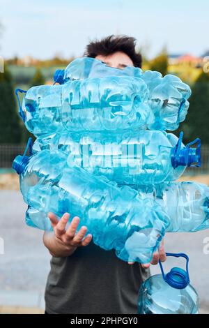 Giovane uomo gettando fuori le bottiglie di acqua di plastica usate vuote nel cestino. Raccolta dei rifiuti in plastica per il riciclaggio. Concetto di inquinamento plastico e troppo ma Foto Stock