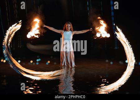 Donna caucasica che balla con il fuoco in acqua. Spettacolo di fuoco in mare. Acrobazie sulla spiaggia. Yoga e relax al tramonto. Spettacolare spettacolo da circo. corpo del modello. Riprese FullHD di alta qualità. Foto Stock