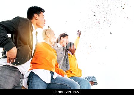 Gruppo multirazziale di persone ha sorpreso all'aperto il giorno di primavera soleggiato sotto la pioggia scintillante. Vista laterale Foto Stock