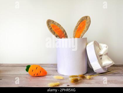 orecchie di coniglio pasquale in una scatola regalo con carota su sfondo di legno Foto Stock