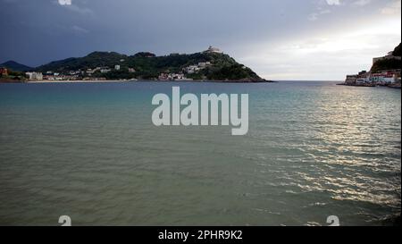 Vista al tramonto della baia di la Concha dalla spiaggia della città, al tramonto, nuvole tempestose sullo sfondo, Donostia-San Sebastian, Gipuzkoa, Spagna Foto Stock