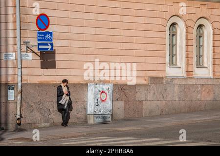 Donna appoggiata contro la fondazione di pietra e la navigazione del telefono cellulare a Hallituskatu nel distretto di Kruununhaka di Helsinki, Finlandia Foto Stock