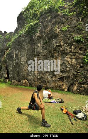 Un arrampicatore di roccia si allunga mentre si sta preparando davanti alla faccia di una collina calcarea per una sessione di arrampicata sportiva in una zona costiera chiamata Siung Beach, che è amministrativamente situato a Duwet, Purwodadi, Tepus, Gunungkidul, Yogyakarta, Indonesia. La spiaggia e' una delle popolari destinazioni ricreative costiere di fronte all'Oceano Indiano nella speciale regione di Yogyakarta. Per gli appassionati di arrampicata su roccia, Siung Beach offre più di 200 percorsi sportivi che sono già stabiliti sulle sue colline calcaree. Foto Stock