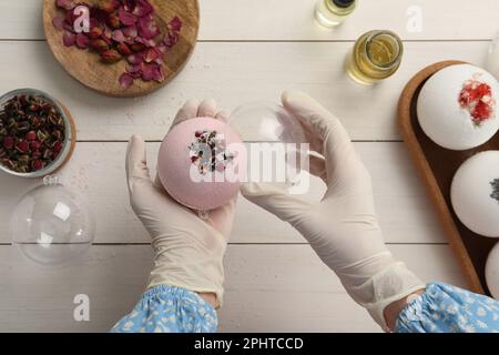 Donna in guanti con bomba da bagno autofabbricata al tavolo bianco, vista dall'alto Foto Stock