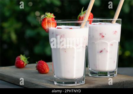 Frullato di fragola in due bicchieri di vetro e fragole fresche su un tavolo di legno nel cortile. Foto Stock