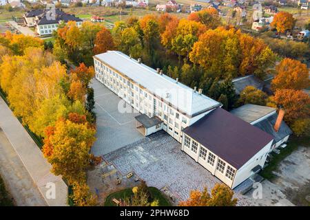 Vista aerea della scuola, del college o dell'asilo con un grande cortile tra alberi autunnali sullo sfondo del paesaggio rurale Foto Stock