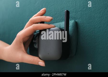 Donna che collega il ripetitore WiFi nero alla presa elettrica sulla parete verde Foto Stock