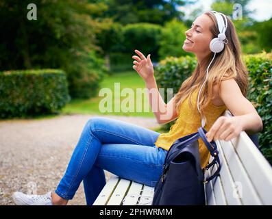 Momenti melodici nel parco. una giovane donna spensierata che ascolta musica su una panchina del parco. Foto Stock