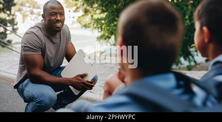 Insegnante che parla con i suoi studenti al di fuori della classe in una scuola elementare. Educatore della scuola elementare che motiva un gruppo di bambini. Tutorship accademica e. Foto Stock