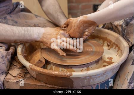 potter insegna al bambino. Un artigiano siede su una panca con una ruota di vasaio e fa una pentola di argilla. Artigianato nazionale. Primo piano delle mani. Foto Stock