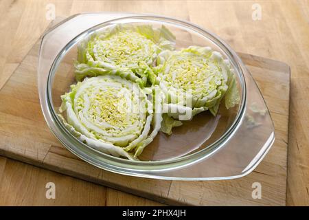 Fette di cavolo di napa o cinese crudo in una casseruola di vetro su un tavolo da cucina di legno preparato per la cottura in forno, cucina vegetariana creativa, il COP Foto Stock