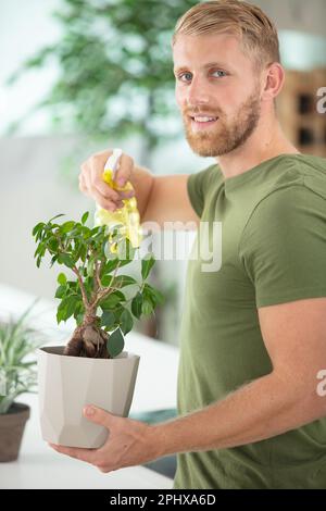 giovane uomo bello spruzzando piante di casa Foto Stock