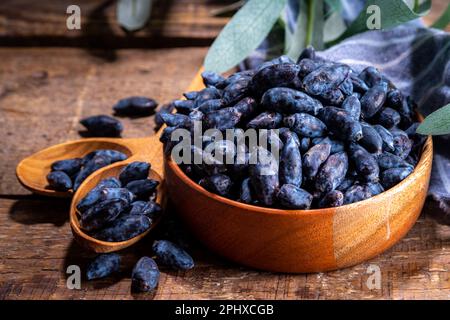 Ciotola con fresco fattoria Haskap bacche, giardino coltivato miele, miele, su sfondo legno copia spazio Foto Stock