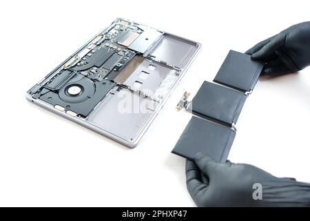 Le mani che indossano guanti in nitrile nero tengono una batteria gonfia appena rimossa dal computer portatile da riparare isolata su bianco. Foto Stock