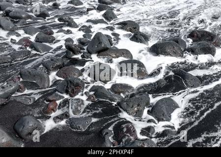 Aspra bellezza di rocce vulcaniche lungo una pittoresca costa oceanica alle Hawaii. Potenti onde d'arresto si rompono contro le rocce, producendo un giacimento schiumoso Foto Stock