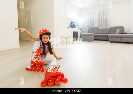 Bambina prescolare seduta indossando i pattini a rotelle e incrociando le gambe Foto Stock