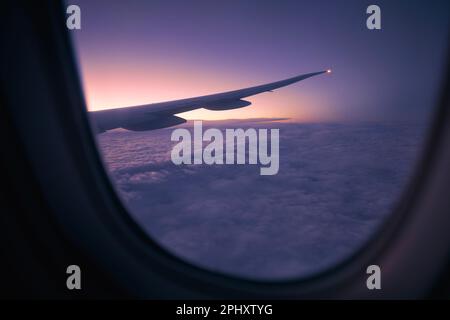 Vista dalla finestra dell'aereo durante il volo sopra le nuvole all'alba. Focalizzazione selettiva sull'ala dell'aeromobile. Foto Stock