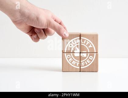 Concetto certificato di qualità. Controllo e garanzia della qualità aziendale. Garanzia e conformità agli standard di qualità. Mano posiziona cubi di legno di qualità certi Foto Stock