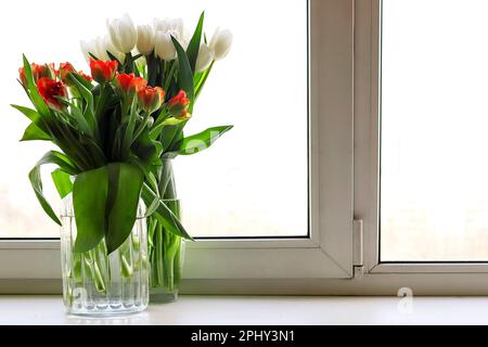 Due bouquet in vasi di vetro di fiori di tulipano rosso e bianco arancio sulla finestra sullo sfondo della città Foto Stock