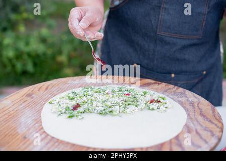 Cuoco femminile, chef che indossa pasta da arrotolare grembiule, mettere il ripieno, versare la salsa, fare pita. Foto Stock