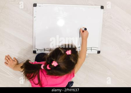 Immagine di ragazza piccola felice seduta vicino a un sacco di matite da colorare su sfondo bianco. Guardando da parte. Foto Stock