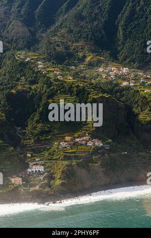 Una pittoresca vista sulla costa di Madeira, caratterizzata da alberi lussureggianti e montagne che si affacciano sul mare blu cristallino. Foto Stock