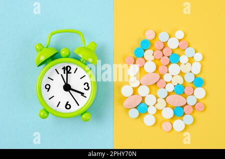 Pillole e sveglia sullo sfondo di colore blu e giallo Foto Stock
