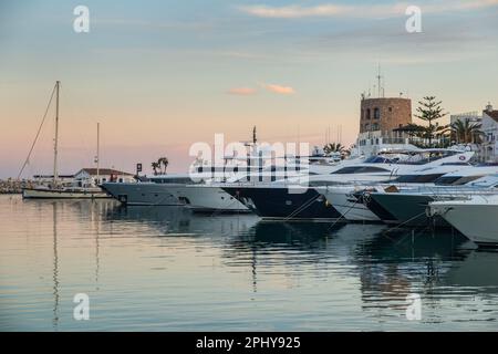 Yacht di lusso alla luce della sera ormeggiati a Puerto Banus Marina, Marbella, Spagna con la torre di controllo marino sullo sfondo Foto Stock