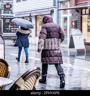 Sandnes, Norvegia, 13 2023 marzo, persone che camminano lungo Sandnes High Street in Heavy Rain in Un giorno d'inverno uno con un ombrello Foto Stock