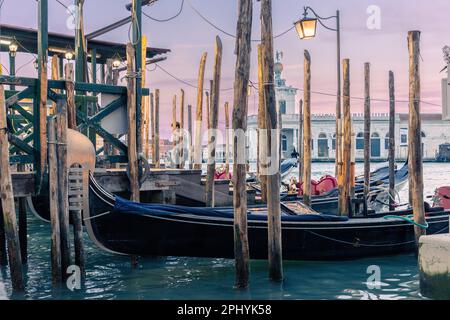 Una gondola ormeggiata vicino a pali di legno lungo un lungomare a Venezia, Italia Foto Stock