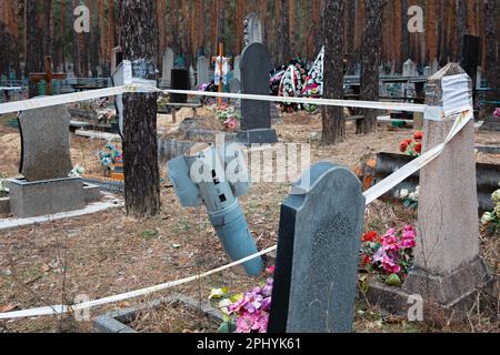 Razzo inesploso recintato per la sicurezza con nastro di avvertimento può essere visto nel cimitero di Izyum, regione di Kharkiv. Izyum nella regione di Kharkiv in Ucraina, sei mesi dopo il ritiro dell'esercito russo. Anche se la città non è più sotto il fuoco, vi è ancora un alto rischio di esplosioni a causa della presenza di mine, tripwire e ordigni inesplosi. Izyum fu liberato il 10 settembre 2022 durante una controffensiva delle forze armate ucraine, ma la città è stata gravemente danneggiata dal bombardamento e dall'occupazione russa, con il 80% degli edifici danneggiati. Tombe di massa di civili ucraini e soldati, inc Foto Stock