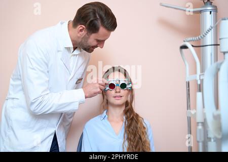 Il bell'optometrista sta esaminando la vista di una paziente donna in un ufficio ottico Foto Stock