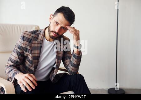Si siede sulla sedia. Uomo d'affari giovane ed elegante in tuta interna. Concezione del successo Foto Stock