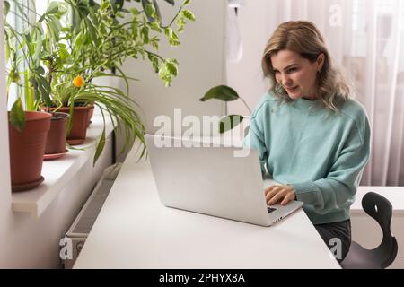 Vista laterale testa scattata sorridente signora freelancer gara mista indossando cuffie, comunicando con il cliente tramite videochiamata al computer. Piacevole millenario Foto Stock