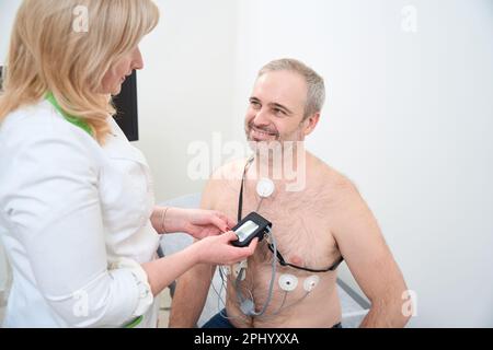 Mano del medico che applica il cardiofrequenzimetro holter sul torace maschile Foto Stock