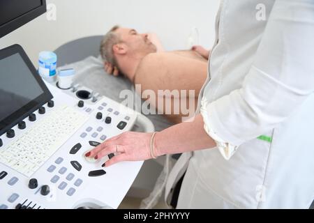 Medico che utilizza un apparecchio a ultrasuoni per eseguire la scansione di un paziente di sesso maschile senior Foto Stock