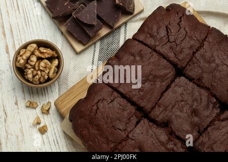 Deliziosi brownie appena sfornati, noci e pezzi di cioccolato su tavola di legno bianco, piatto Foto Stock