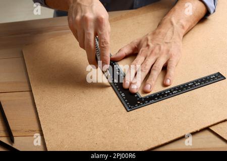 Uomo che taglia il bordo del truciolo con il coltello di utilità ed il righello al tavolo, primo piano Foto Stock