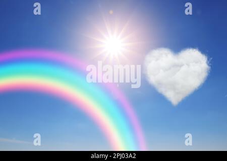 Bella vista di nuvola a forma di cuore, arcobaleno e sole nel cielo blu Foto Stock