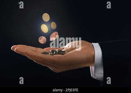 Uomo e monete che cadono in mano su sfondo nero, primo piano Foto Stock