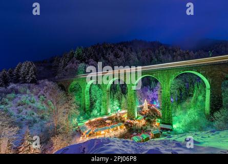 Mercatino di Natale nella Gola di Ravenna nella Foresta Nera innevata, il viadotto ferroviario della Hoellentalbahn è illuminato con colori vivaci, Foresta Nera Foto Stock