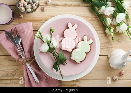 Tavolo per brunch pasquale. Concetto di vacanza di Pasqua di primavera con piatto bianco, rosa e tovagliolo con simboli decorativi di festa coniglio, uova e bouquet Foto Stock
